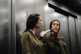 A young woman in an elevator blowing a kiss to herself in the mirror