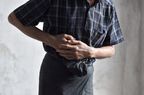 Close up of the torso of a man wearing a plaid shirt, holding the right side of his abdomen in pain, possibly due to hepatitis or another health condition.