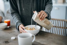 Person pouring milk into a cereal bowl in a home kitchen