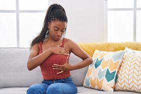 A woman does a breast exam while sitting on her couch.