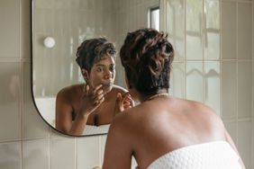 woman looking closely into bathroom mirror