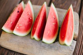 Five slices of red watermelon on a cutting board, sitting on a dark wooden table.