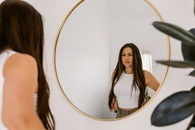 Attractive hispanic stylish woman looking at herself in a decorative circular mirror from her minimalist home decorated with natural house plants