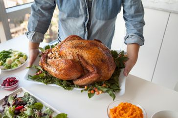 person holding a tray of a cooked full turkey