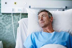 A man in an hospital gown lies in a hospital bed
