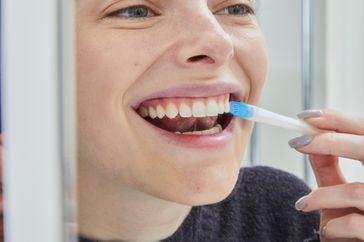 Person using a teeth whitening emulsion on upper teeth