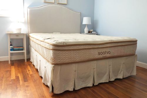 A bare Saatva Classic mattress on a bed frame in a bedroom