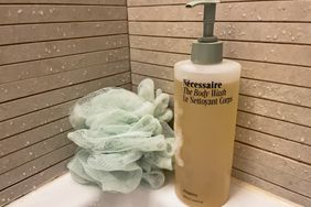 A bottle of Necessaire The Body Wash next to a loofah