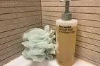 A bottle of Necessaire The Body Wash next to a loofah
