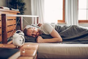 A man in bed with an alarm in the nightstand next to him