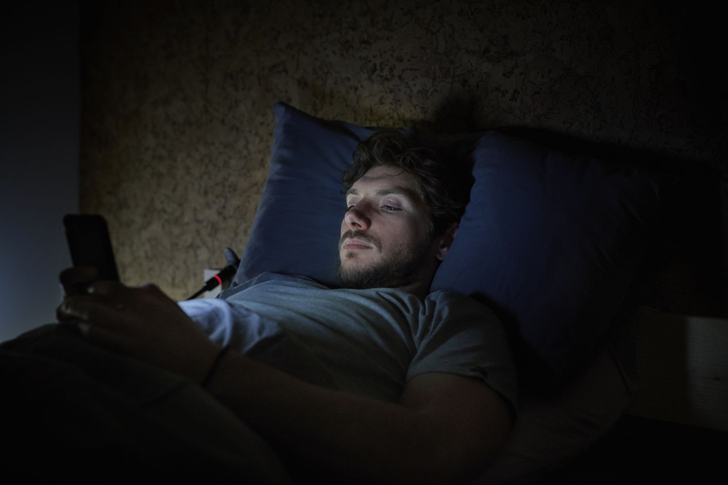 A man on his phone in bed experiencing insomnia