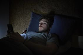 A man on his phone in bed experiencing insomnia