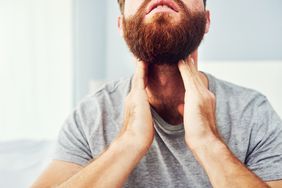 A man touches his throat with both hands