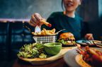 Cropped shot of young Asian woman eating freshly made delicious burger, dipping fries in ketchup on the dining table. 