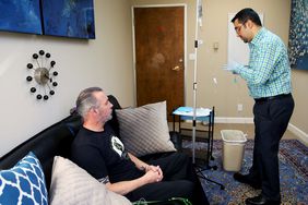 A Doctor Prepares a Ketamine IV Drip in a Clinic room while Patient Sits on a Couch
