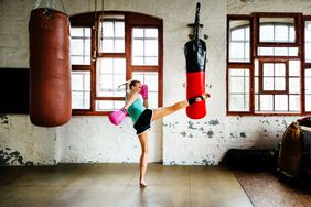 A woman practicing kickboxing, kicking a sandbag at an indoor gym