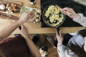 Overhead view of couple cooking scramble eggs together.