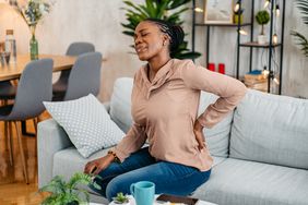 person experiencing lower left back pain while sitting on the couch