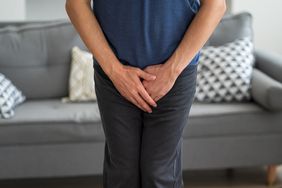 A man standing with both hands over this crotch