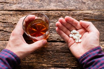A man holding a glass of alcohol and a handful of pills