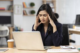 woman sitting at her desk feeling migraine symptoms 