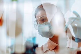 shot of female scientist through window glass sitting and working at a laboratory table