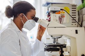 Female microbiologist using a microscope. Female biochemist working in high-tech lab.
