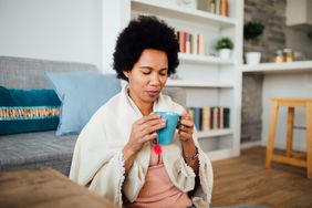 A woman sits with her eyes closed, holding a cup of tea
