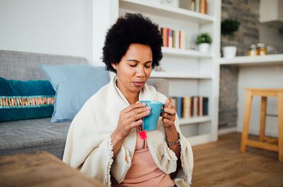 A woman sits with her eyes closed, holding a cup of tea