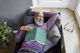 A black man taking a power nap on a couch with a book on his chest