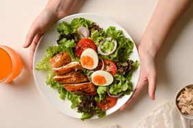 A woman hands serving a plate of fresh roasted chicken fillet with salad vegetables on a white table