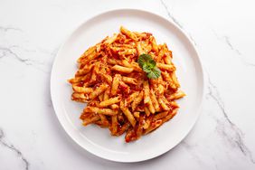 Top view of penne with tomato sauce and cheese on marble surface