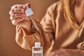 A woman in a beige dress holds a pipette with a drop of retinol serum