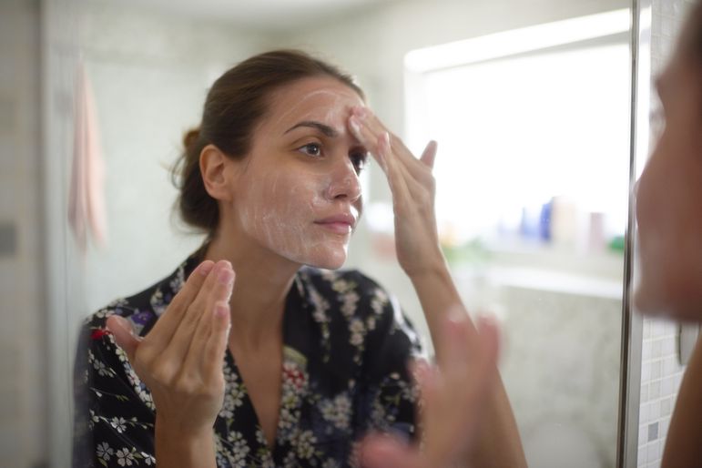 Woman looking at herself in the bathroom mirror while applying a moisturizing cream to her face