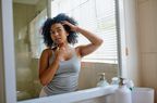 A young black woman inspecting her skin in the bathroom mirror