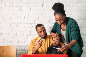 A father holding his little girl in his lap while a mother is checking her temperature