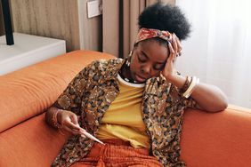 woman on couch with fever and headache holding a thermometer