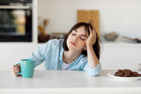 young woman falling asleep on kitchen counter with mug in her hand