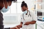 Photo of a female doctor with a protective face mask checking her patient's blood glucose level