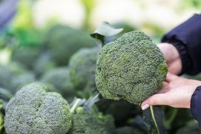A woman shopping for different types of broccoli in the grocery store