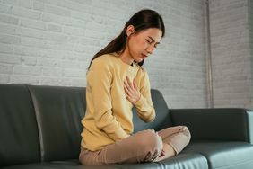 Woman with a yellow sweater sitting on a couch experiencing heartburn on the chest
