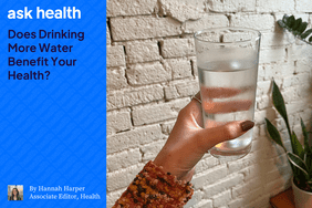 hand holding a glass of cold water in front of a white brick wall